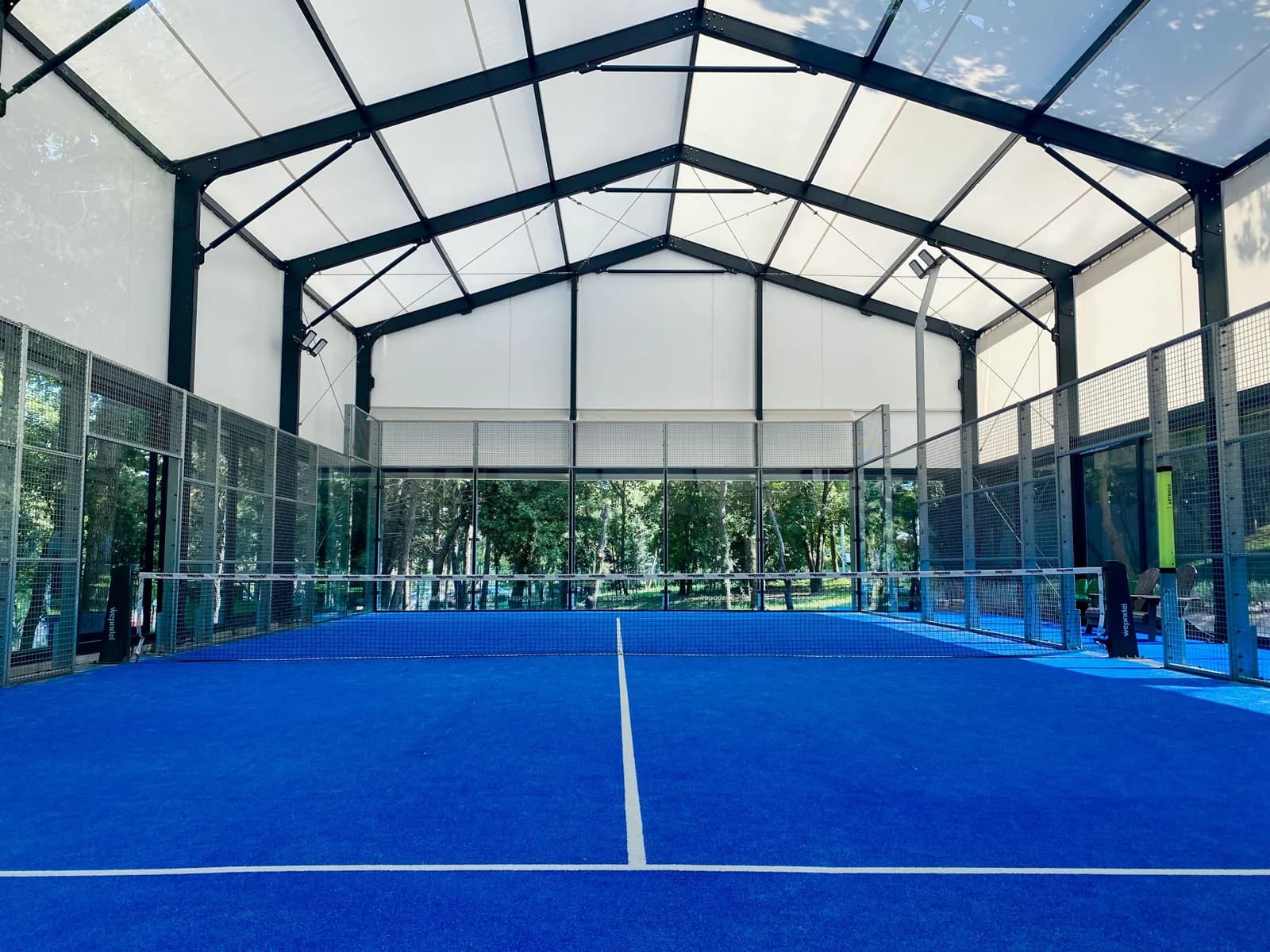 Court de padel bleu sous une couverture lumineuse, ouvert sur la végétation
