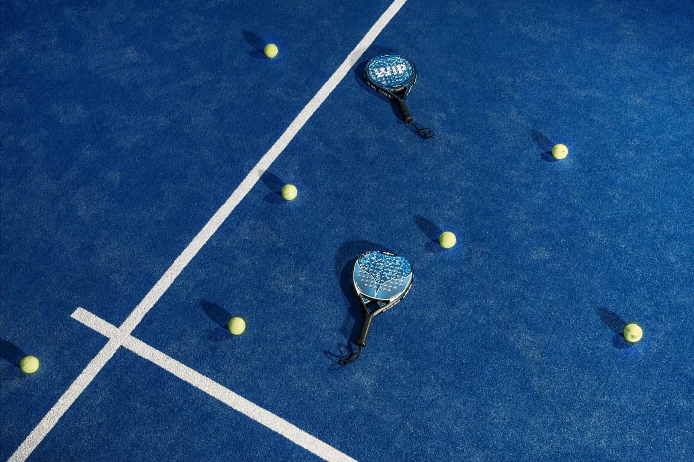 Raquettes et balles sur un gazon bleu de padel, au croisement des lignes de jeu
