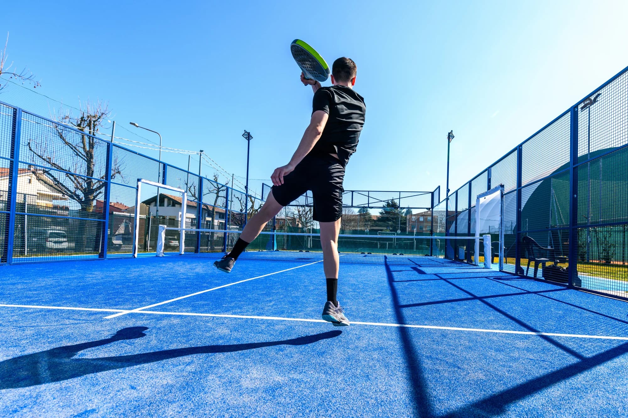 Joueur de padel en plein échange sur un court extérieur bleu ensoleillé