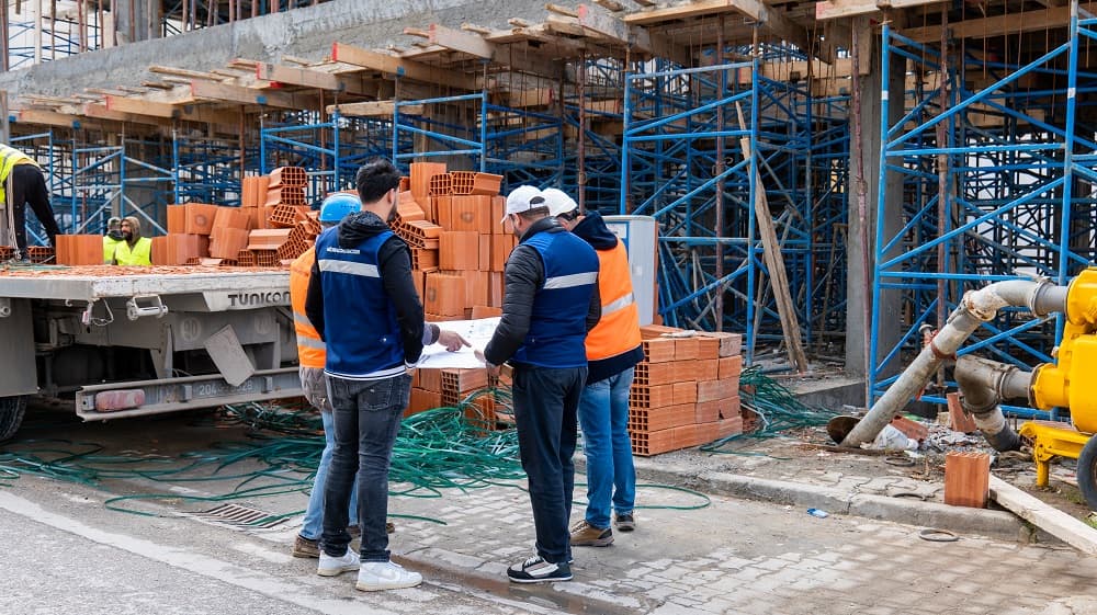 Équipe portant les vêtements Medina Construction devant une structure en béton et des murs en briques