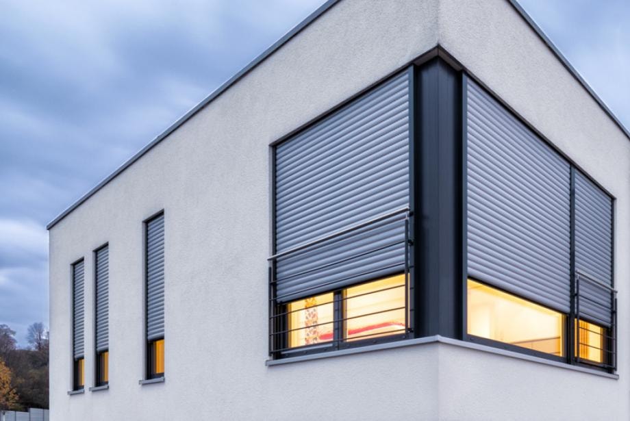 Façade contemporaine avec plusieurs volets roulants gris partiellement fermés